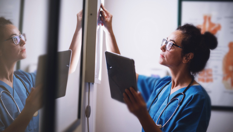 Nurse using an iPad and looking at an x-ray screen