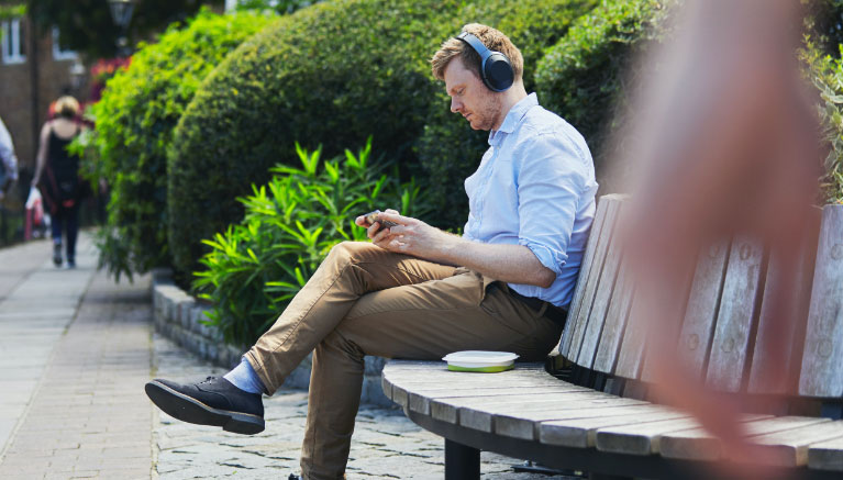 Man sitting on a bench using device with headphones on